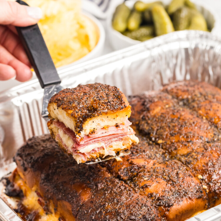 Close-up of a baked ham and cheese slider being lifted, showing melted cheese and layers inside.