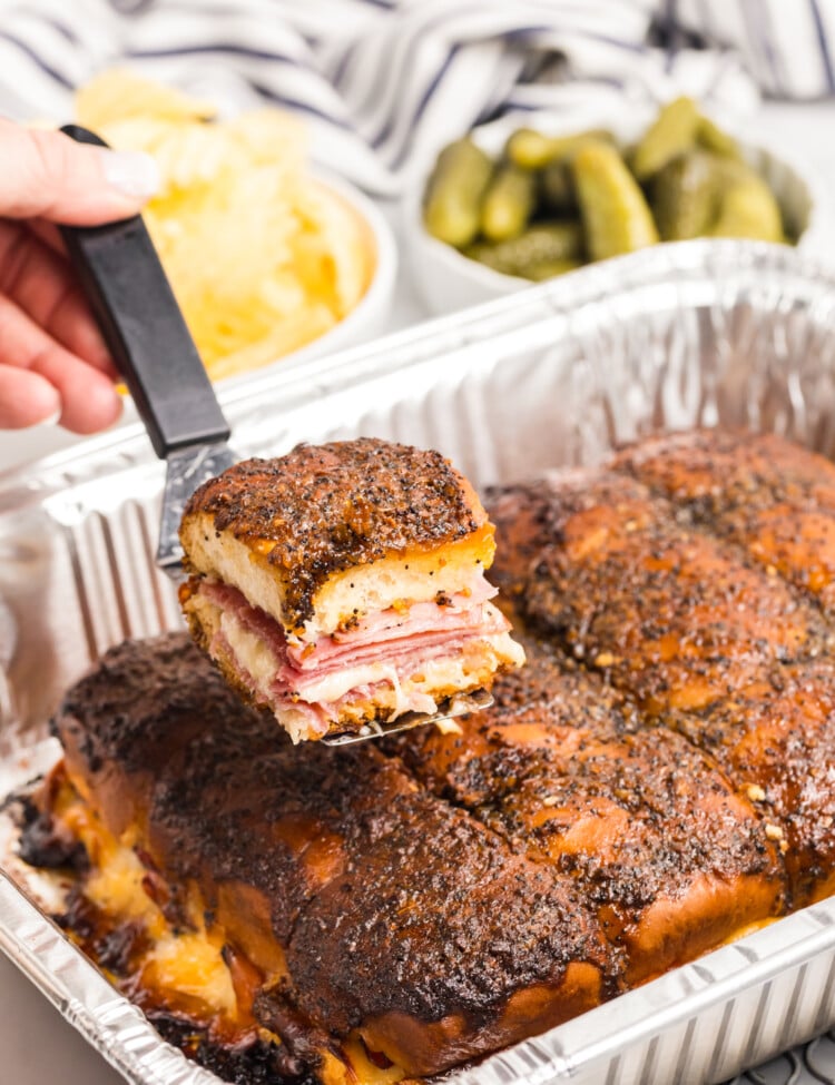 Close-up of a baked ham and cheese slider being lifted, showing melted cheese and layers inside.
