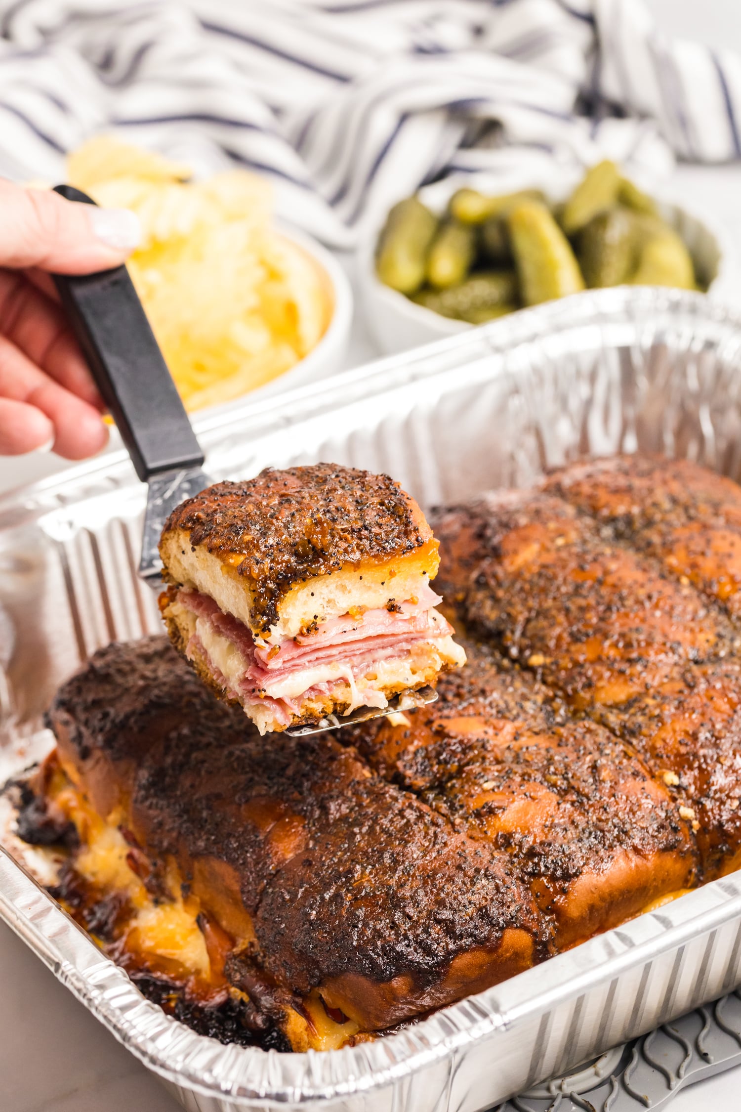 Close-up of a baked ham and cheese slider being lifted, showing melted cheese and layers inside.