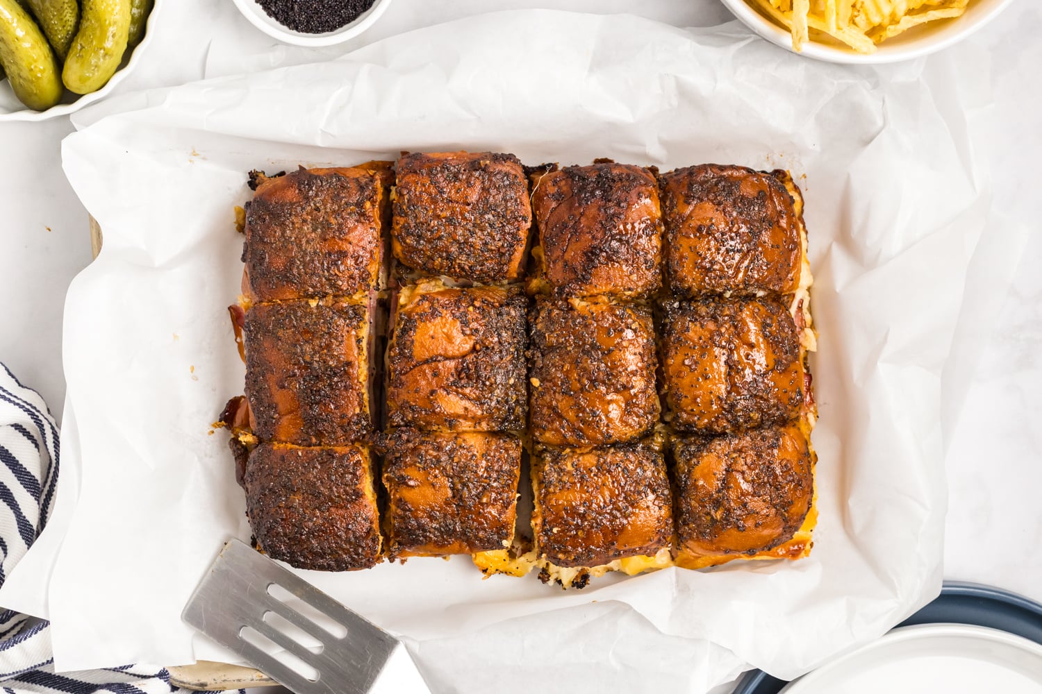 Overhead view of baked ham and cheese sliders cut into portions, with a browned, seasoned topping.