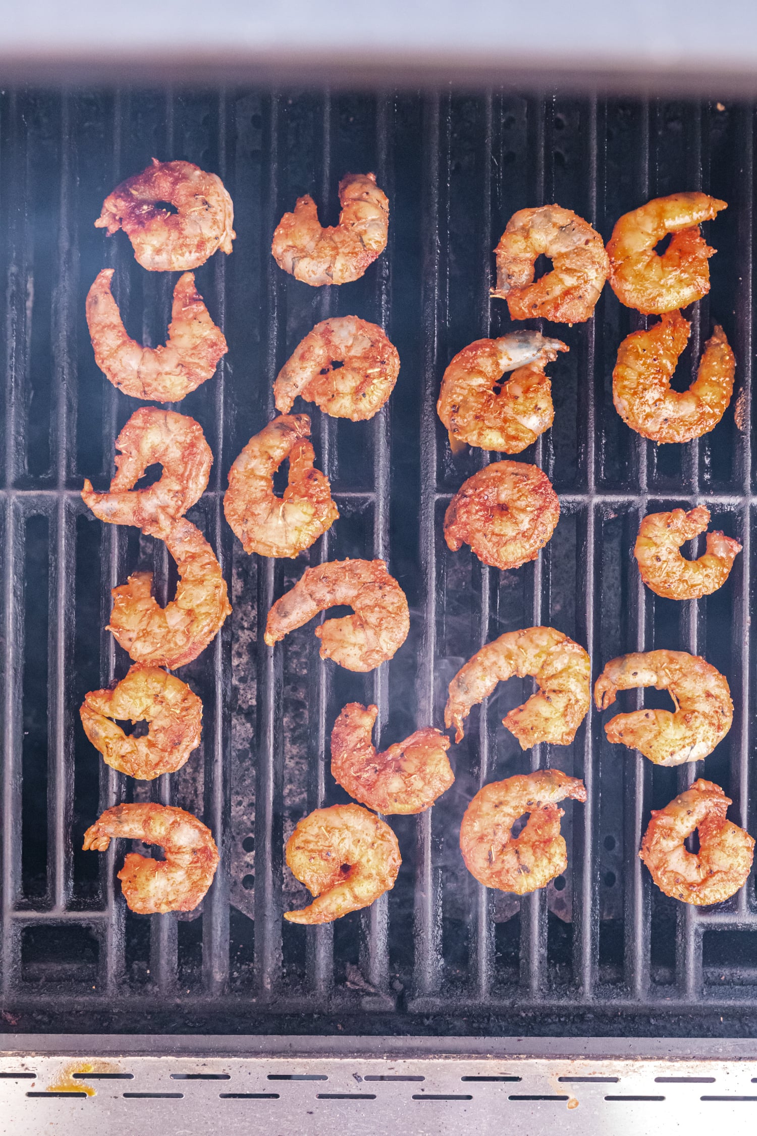 Spiced shrimp cooking on a grill, arranged in rows with visible grill marks.