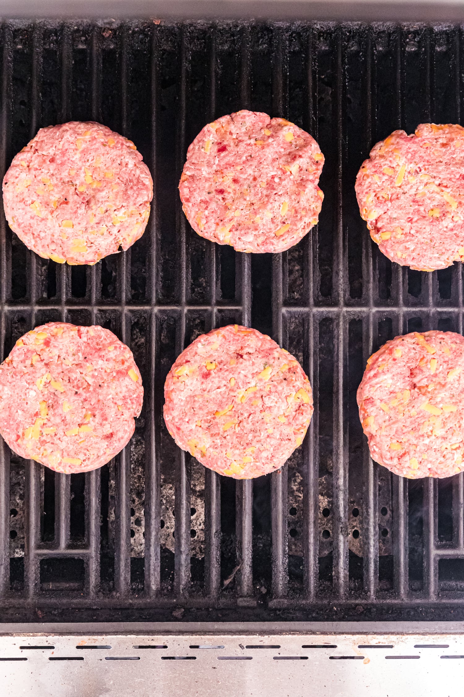 Several raw burger patties cooking on a grill, evenly spaced across the grates.