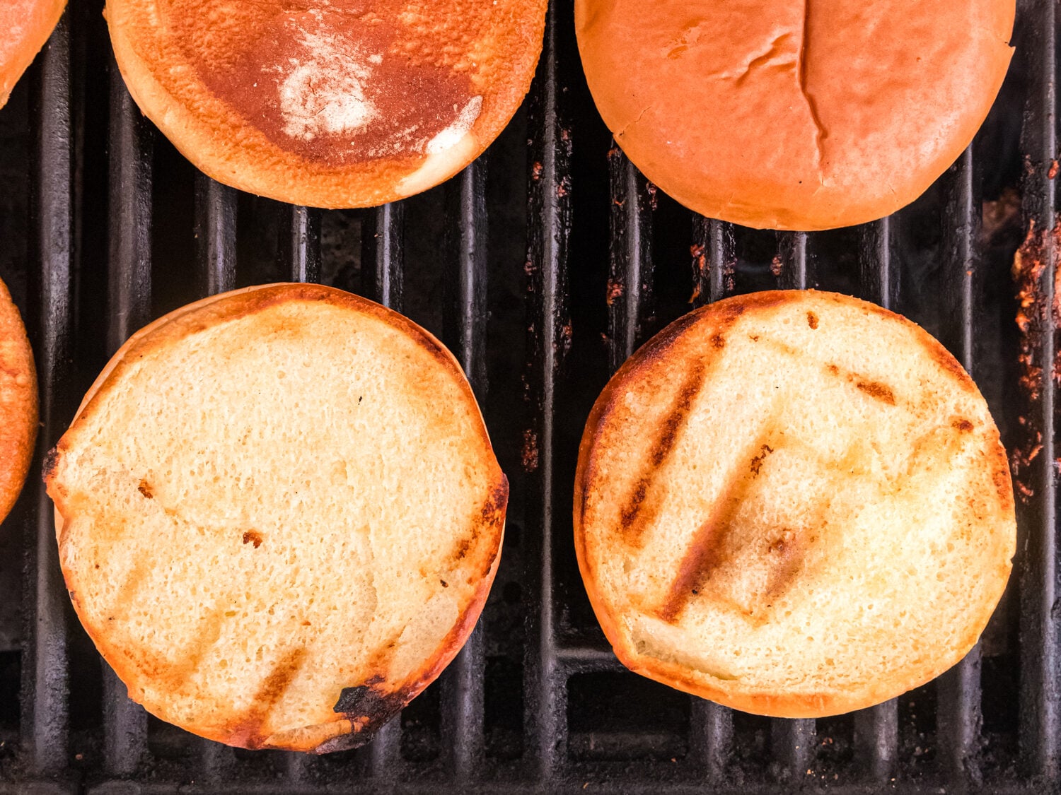 Burger buns toasting on a grill, with golden-brown surfaces and visible grill marks.