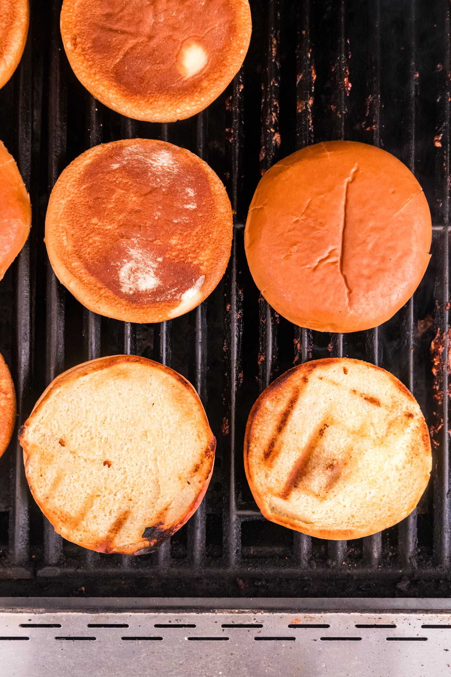 Burger buns toasting on a grill, with golden-brown surfaces and visible grill marks.