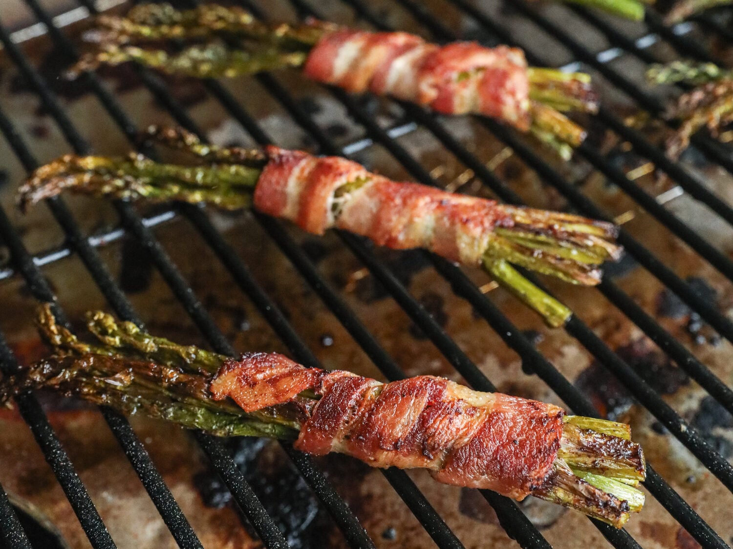 Bacon-wrapped asparagus bundles grilling, with the bacon starting to crisp and brown, and asparagus charring slightly.