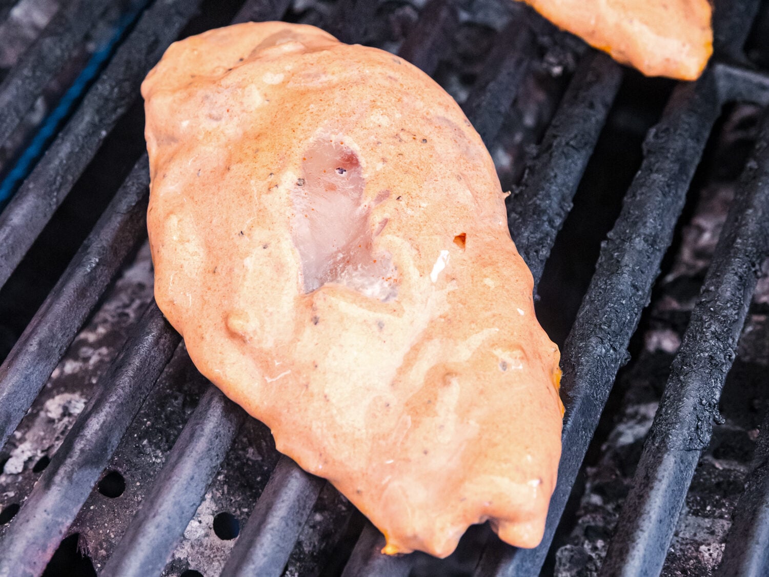 Marinated chicken breasts cooking on a grill, coated in a creamy orange-colored seasoning mixture before developing grill marks.