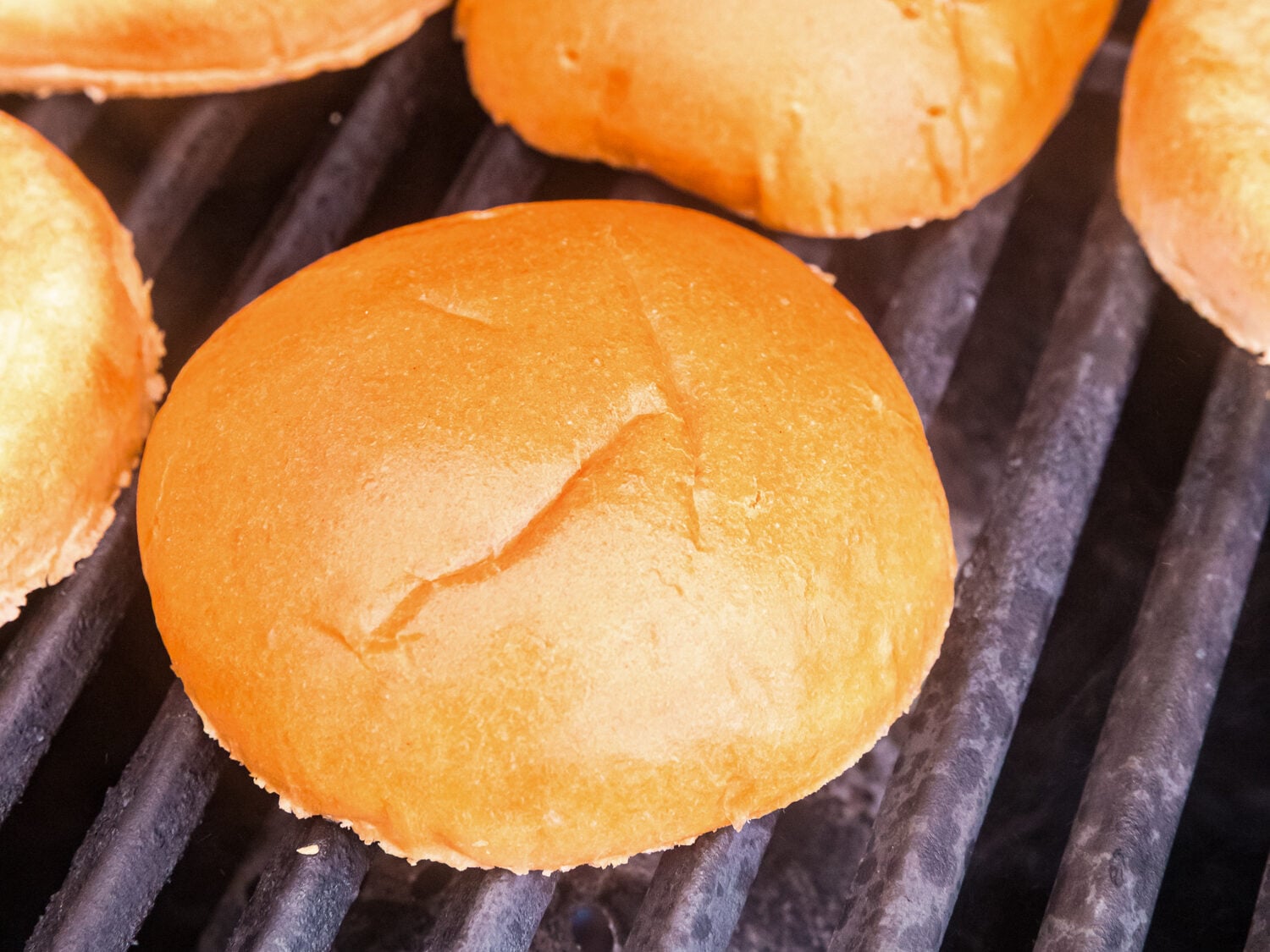 Butter-toasted burger buns warming on a grill, showing golden-brown surfaces ready for assembling burgers.