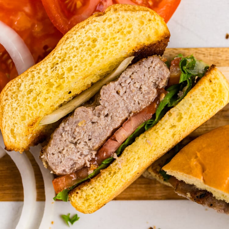 Close-up of a grilled pork burger cut in half, layered with lettuce, tomato, onion, and a juicy pork patty on a toasted bun.