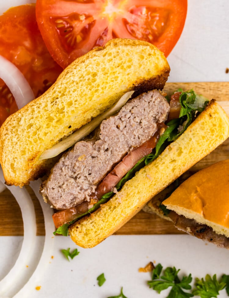 Close-up of a grilled pork burger cut in half, layered with lettuce, tomato, onion, and a juicy pork patty on a toasted bun.