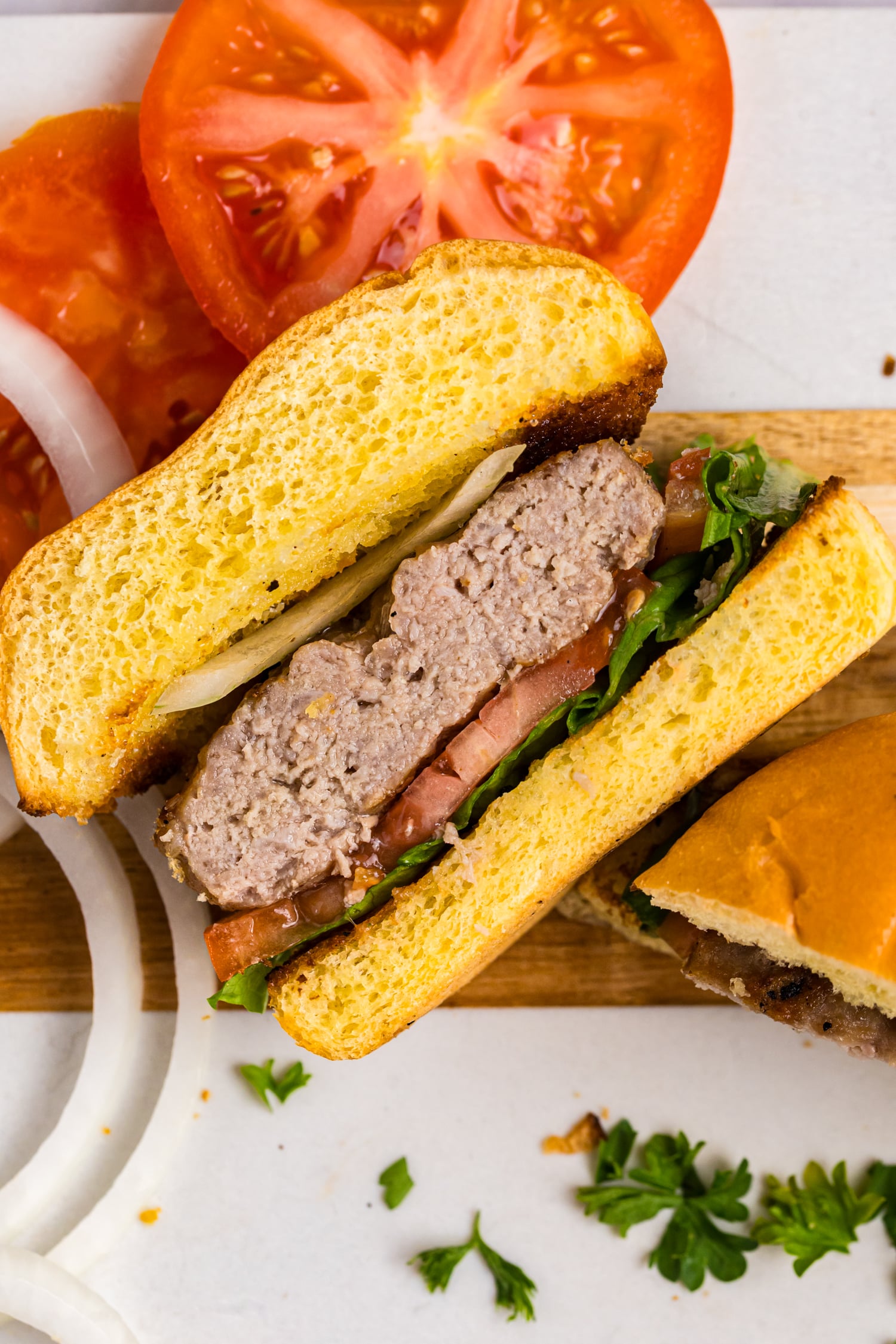 Close-up of a grilled pork burger cut in half, layered with lettuce, tomato, onion, and a juicy pork patty on a toasted bun.