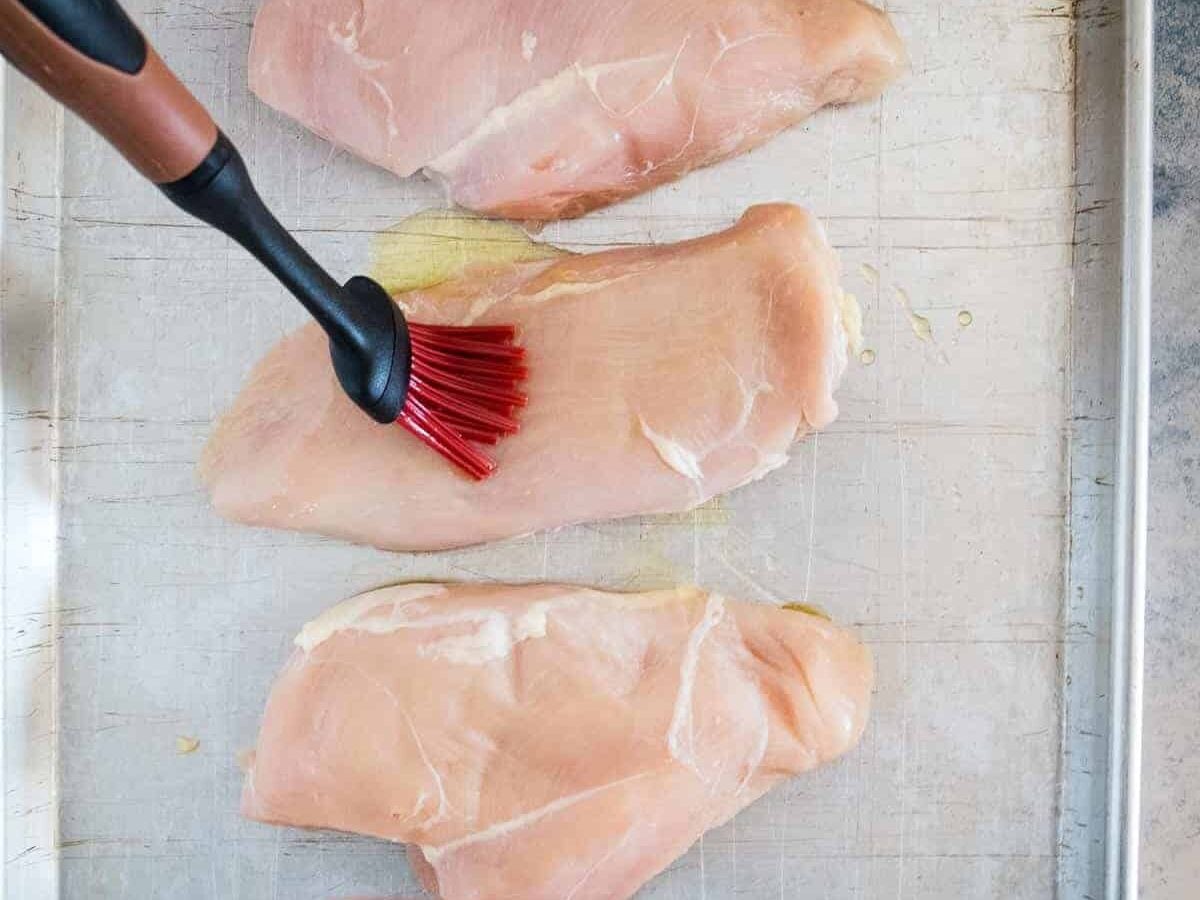 Basting brush putting olive oil on chicken breast