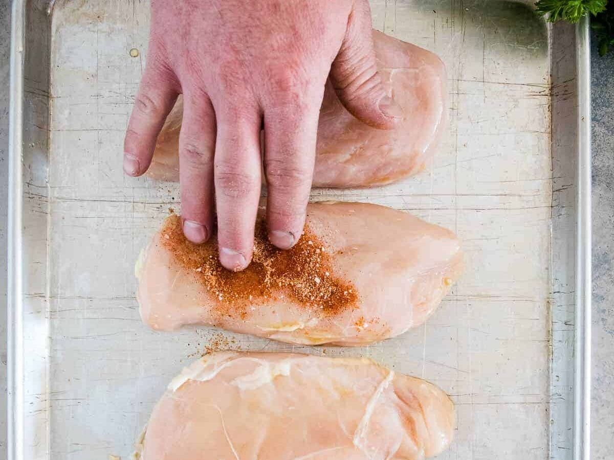 Hand putting seasoning on chicken breast