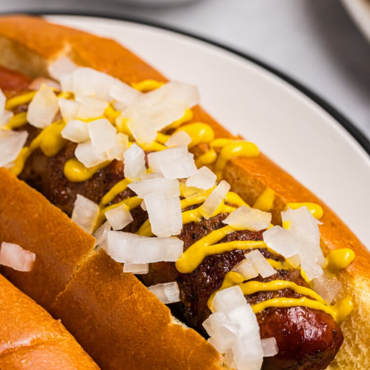 Grilled bacon wrapped hot dog served in a toasted bun with yellow mustard and diced onions.
