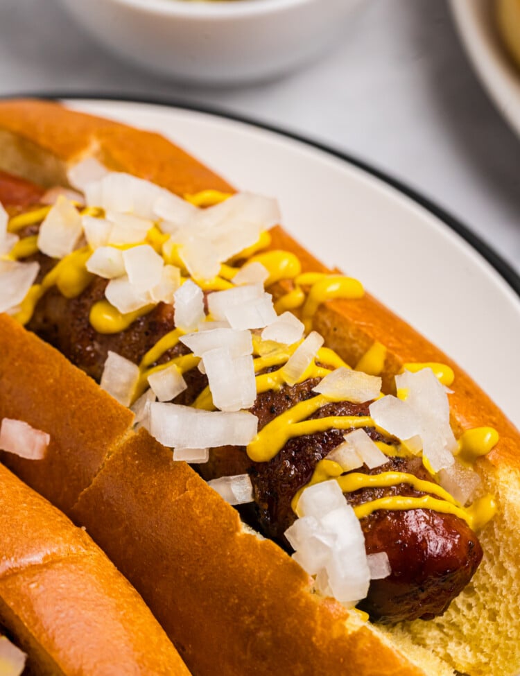Grilled bacon wrapped hot dog served in a toasted bun with yellow mustard and diced onions.