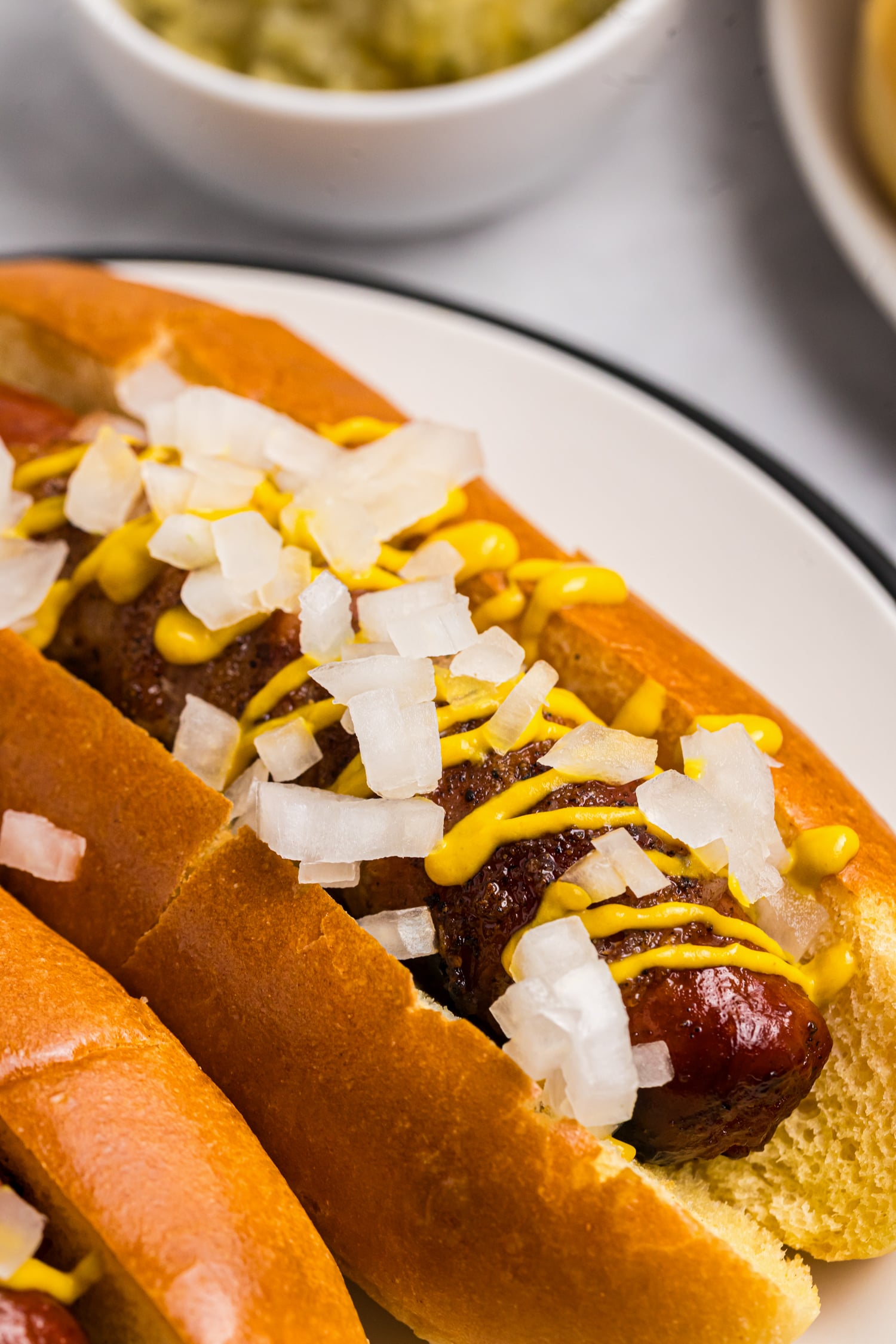 Grilled bacon wrapped hot dog served in a toasted bun with yellow mustard and diced onions.