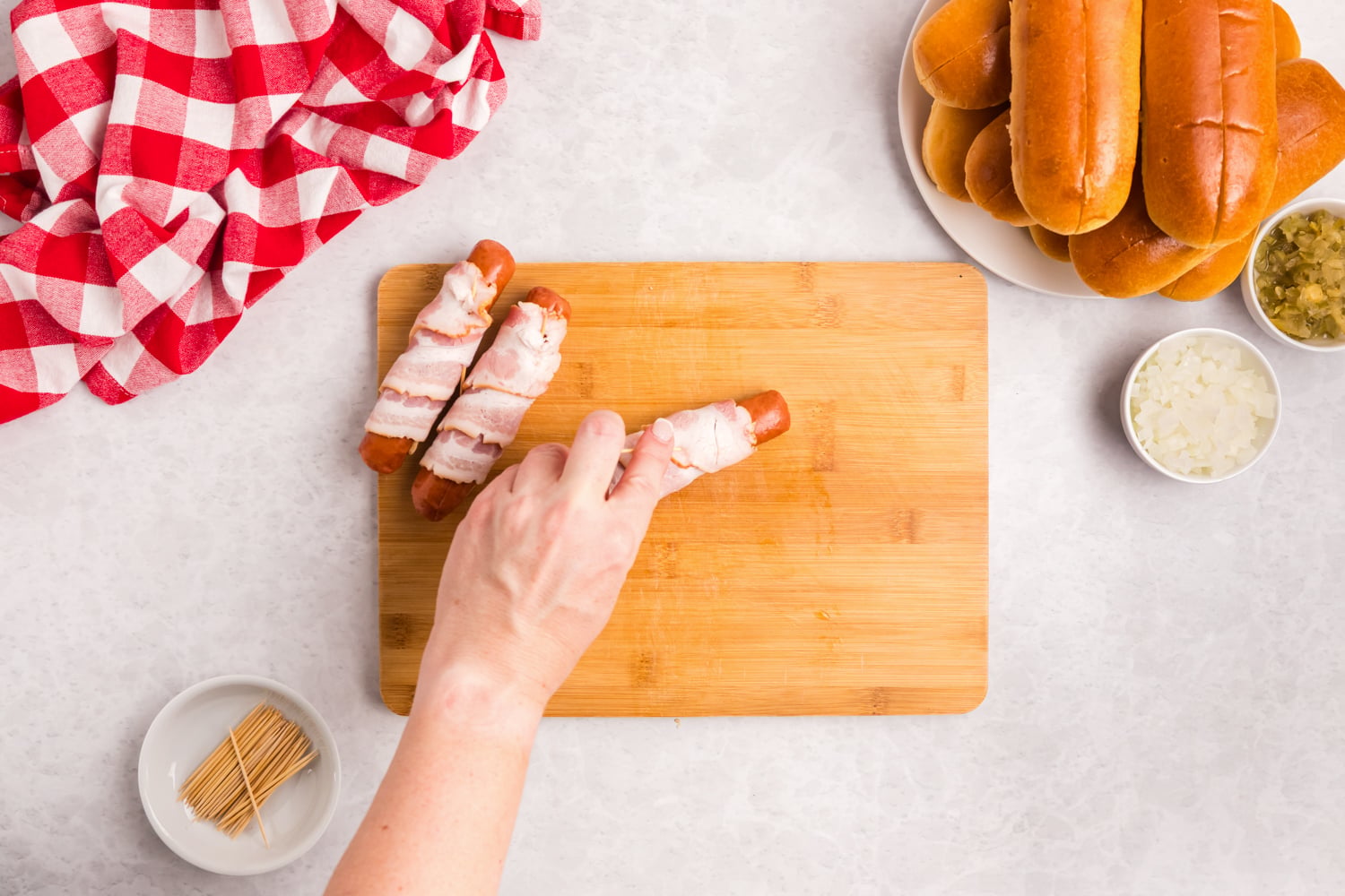 Bacon wrapped hot dogs secured with toothpicks and ready to be seasoned before grilling.