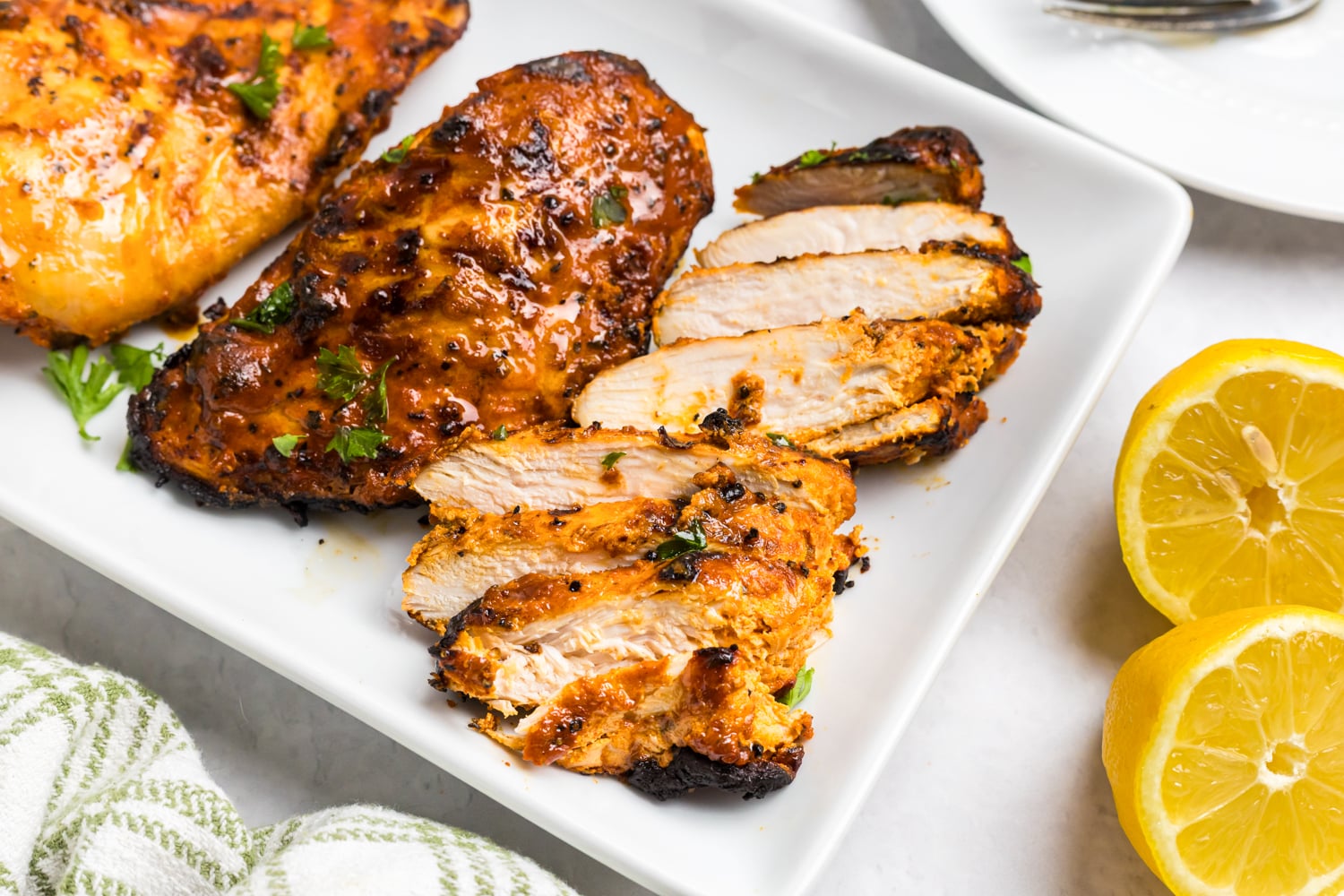 Juicy grilled Mediterranean chicken breast sliced and arranged on a serving platter, garnished with parsley and served with fresh lemon halves.