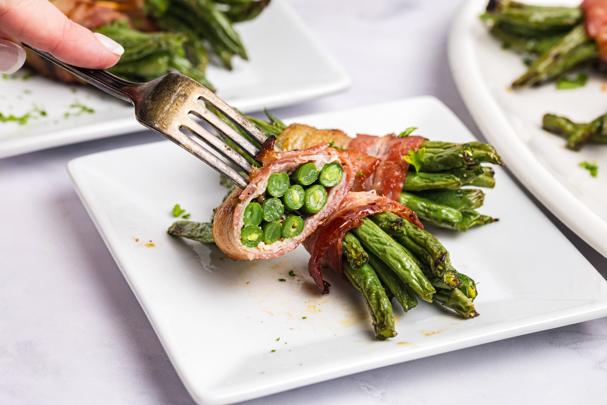Close-up of a bacon-wrapped green bean bundle held on a fork, showing the tender green beans inside the crispy grilled bacon.