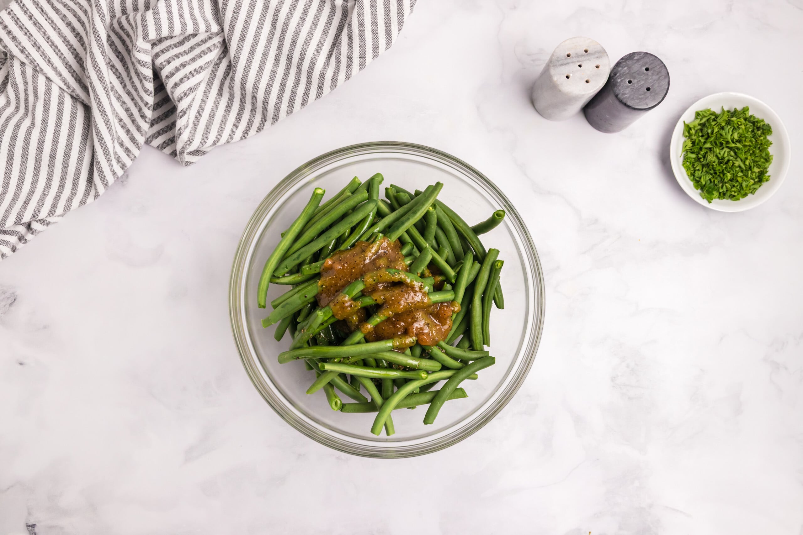 Fresh green beans tossed with a brown seasoning mixture in a clear glass bowl.
