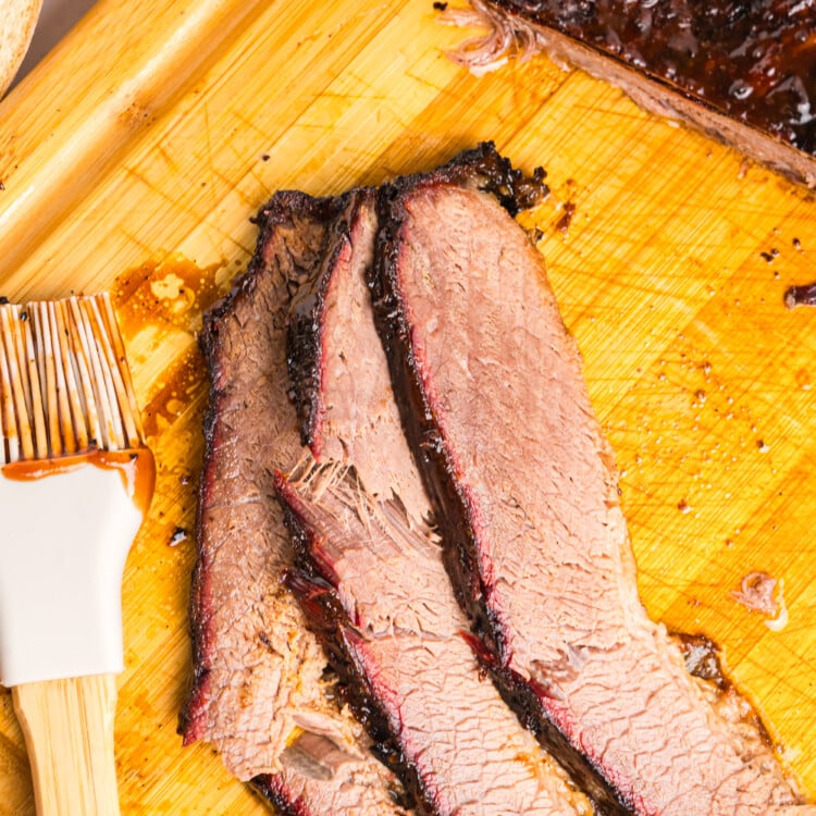 Tender smoked brisket sliced on a cutting board with a dark bark and smoke ring.