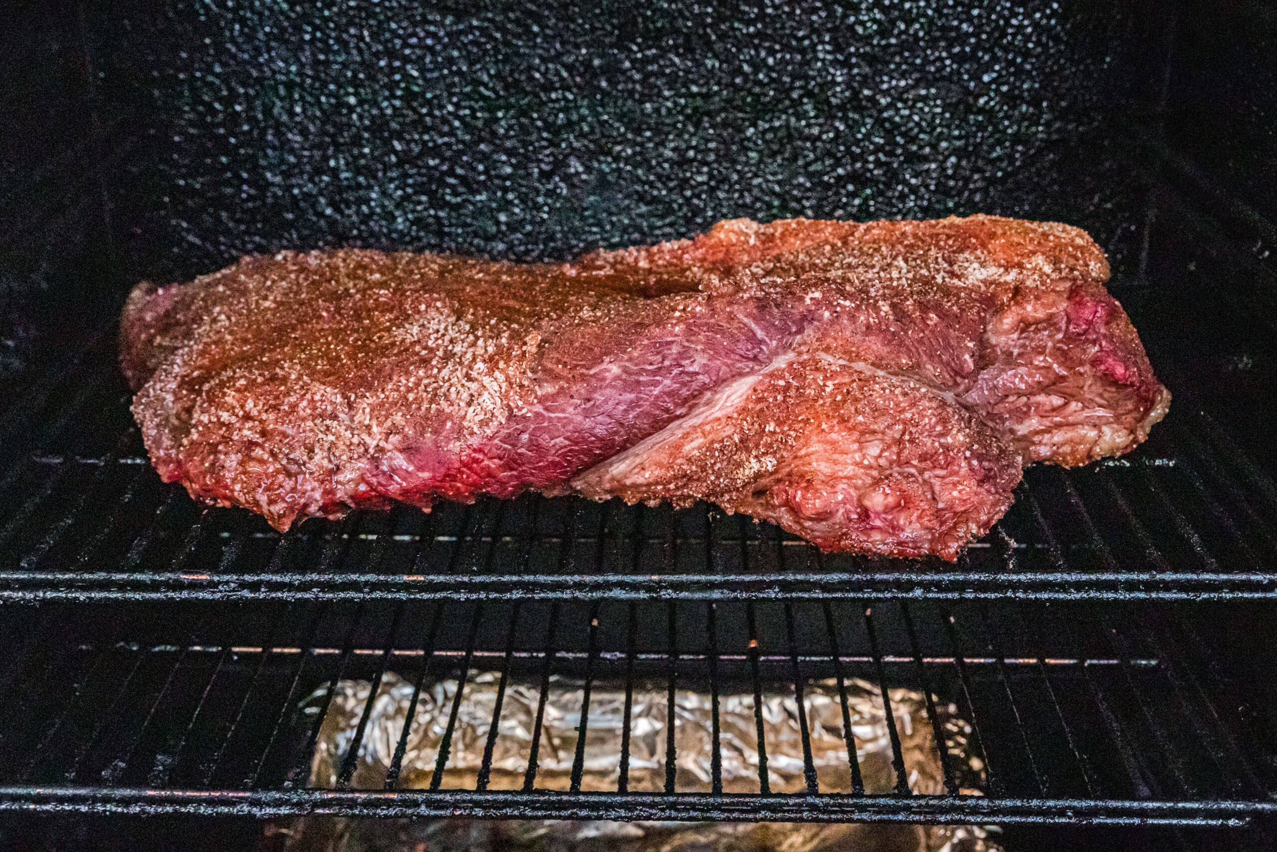 Seasoned beef brisket cooking on the grates inside a smoker.