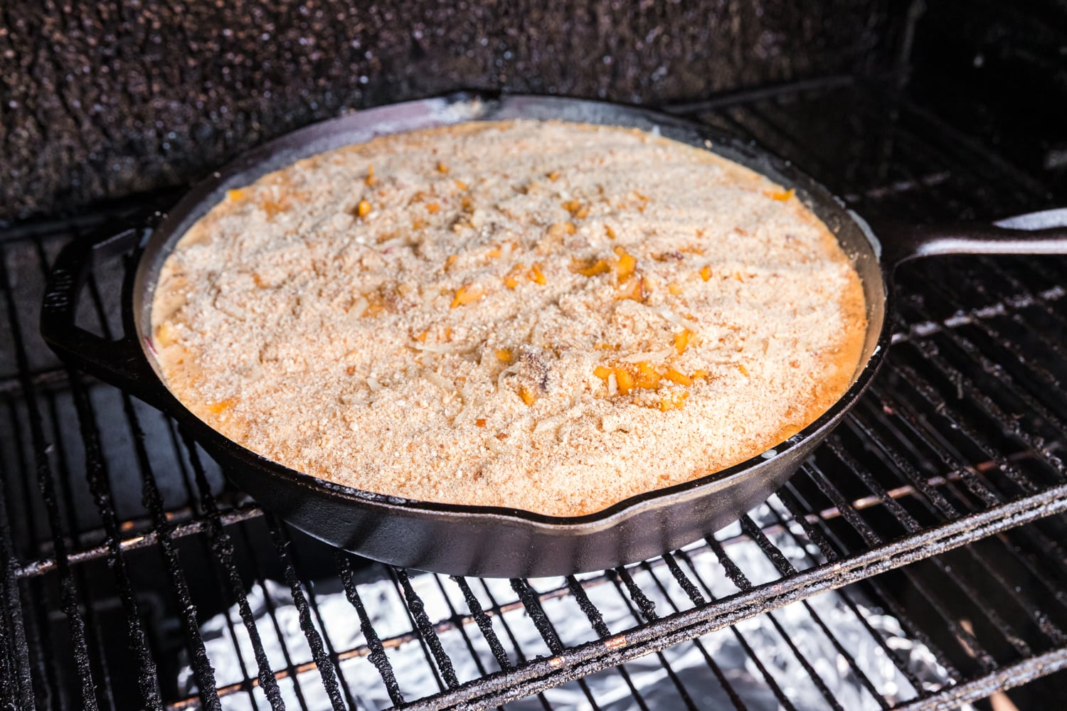 Brisket mac and cheese topped with breadcrumbs and cheese cooking in a smoker.