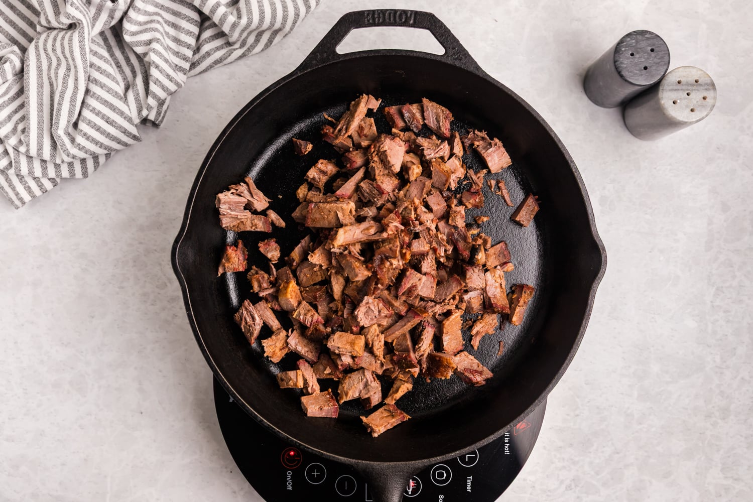 Chopped smoked brisket heating in a cast iron skillet.