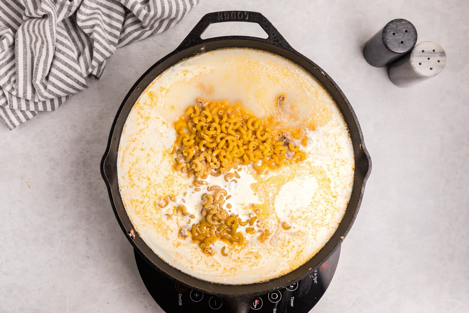 Elbow macaroni added to a creamy cheese sauce in a cast iron skillet.