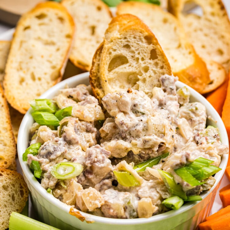 Creamy Philly cheesesteak dip topped with green onions and served with toasted bread, celery and carrots.