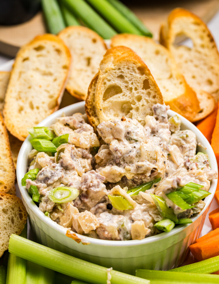 Creamy Philly cheesesteak dip topped with green onions and served with toasted bread, celery and carrots.