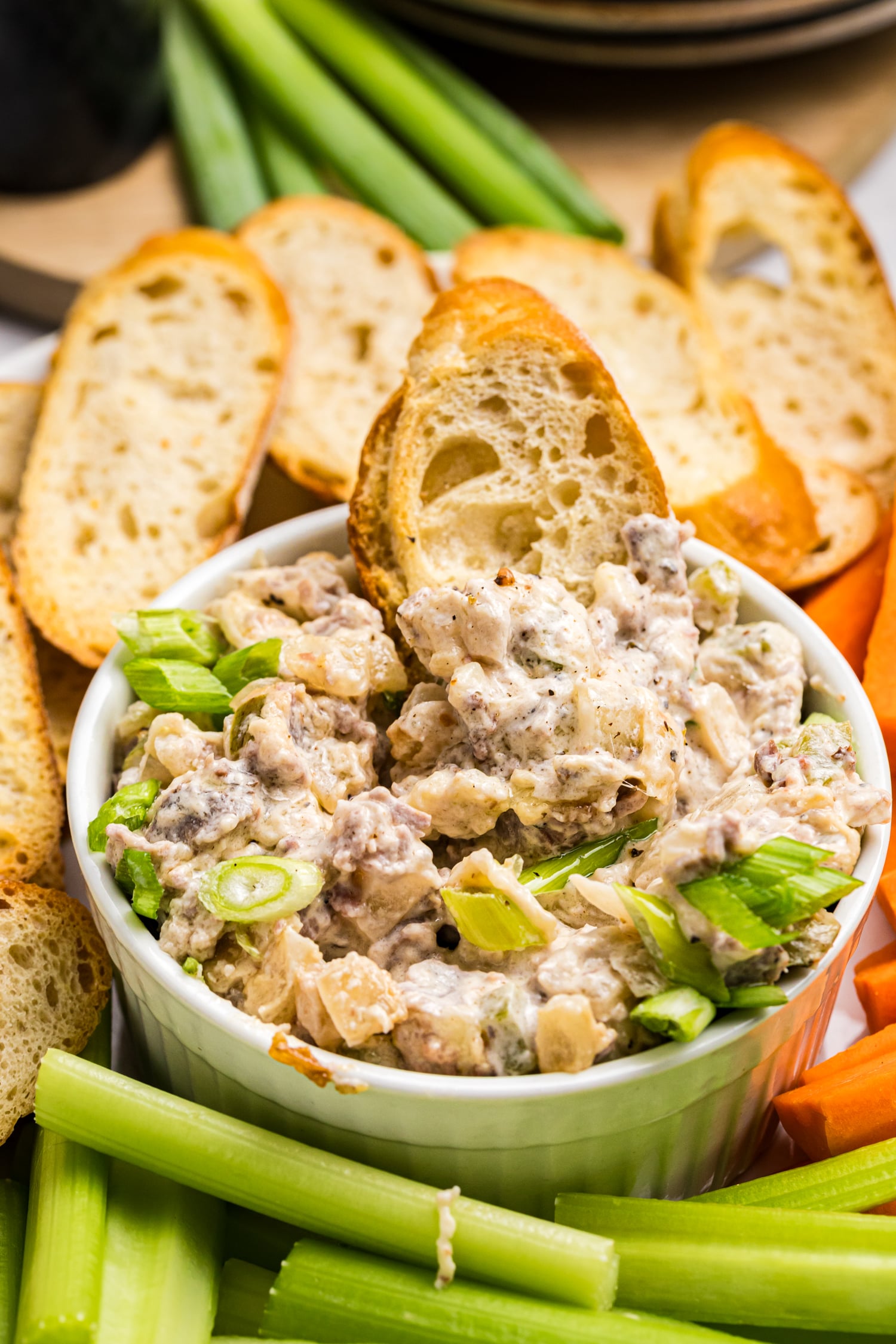 Creamy Philly cheesesteak dip topped with green onions and served with toasted bread, celery and carrots.