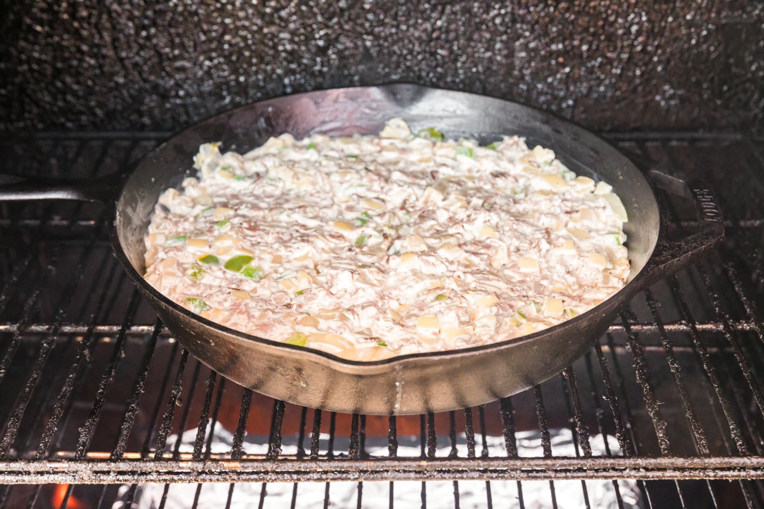 Creamy Philly cheesesteak dip cooking in a cast iron skillet inside a smoker.