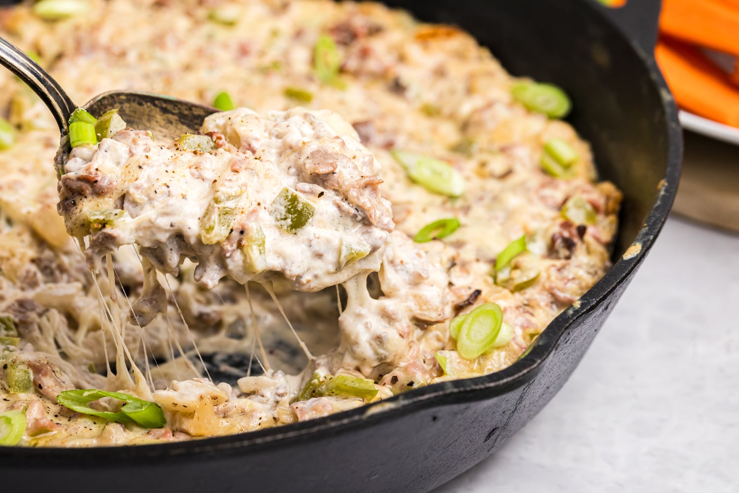 Hot, cheesy Philly cheesesteak dip with beef, peppers and green onions being scooped from a skillet.