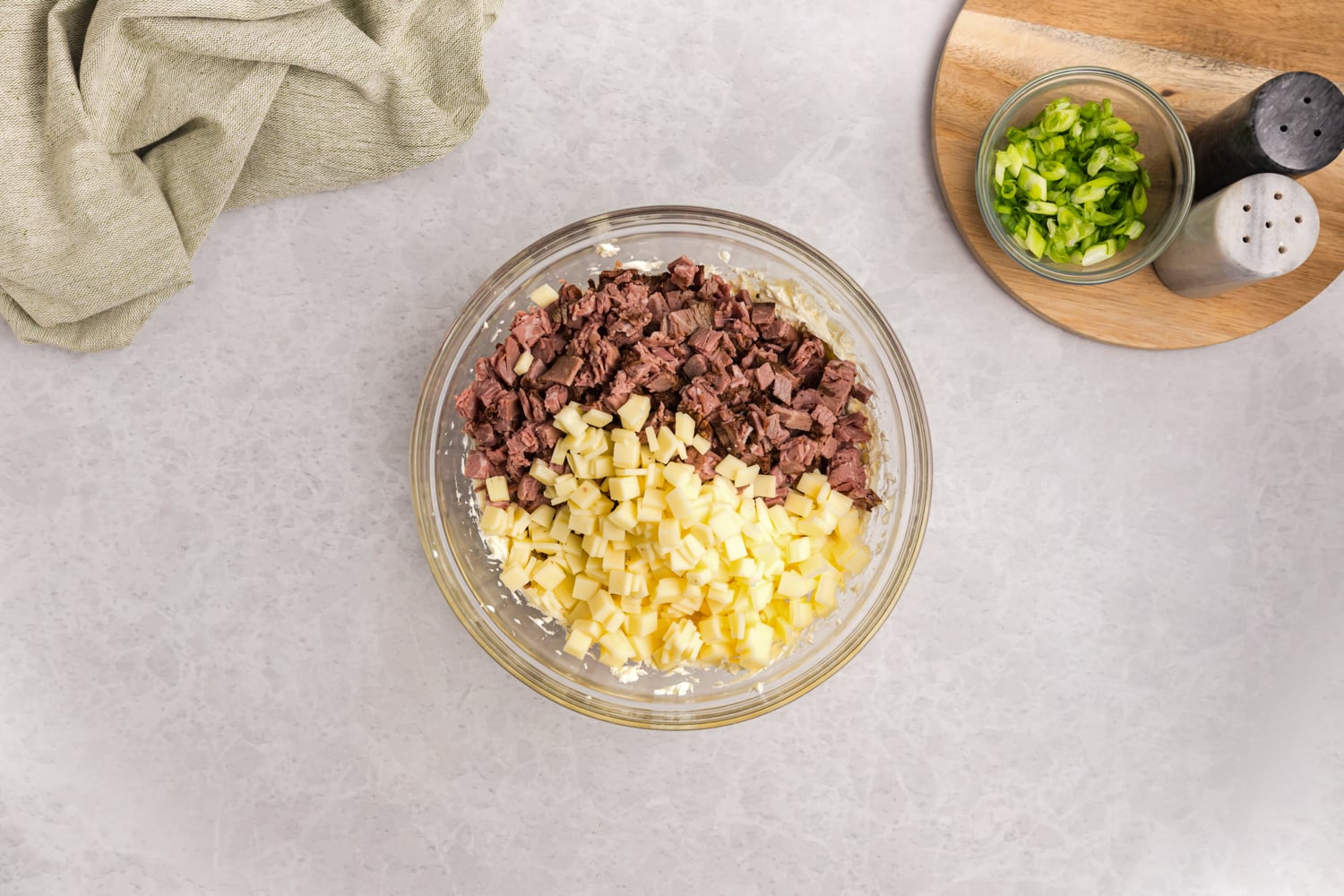 Chopped beef and diced cheese added to a creamy dip mixture in a glass bowl.