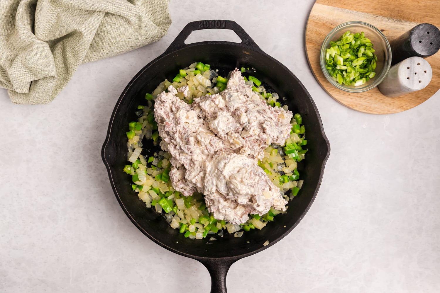 Creamy beef mixture added to sautéed onions and green peppers in a cast iron skillet.