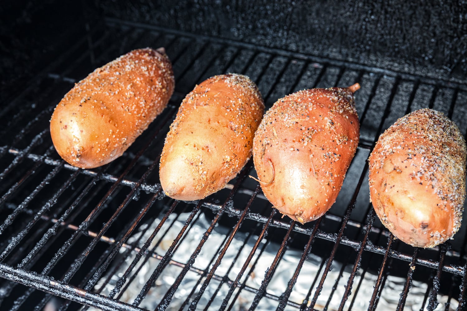 Seasoned whole sweet potatoes cooking directly on the smoker grates.