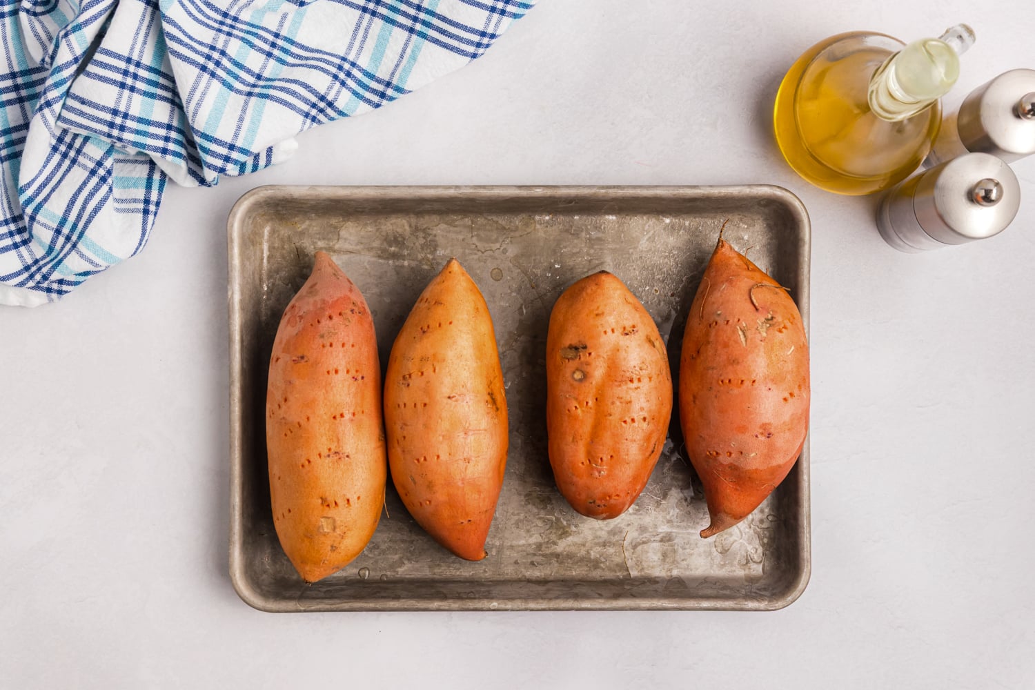 Whole sweet potatoes pierced with a fork and arranged on a baking sheet.