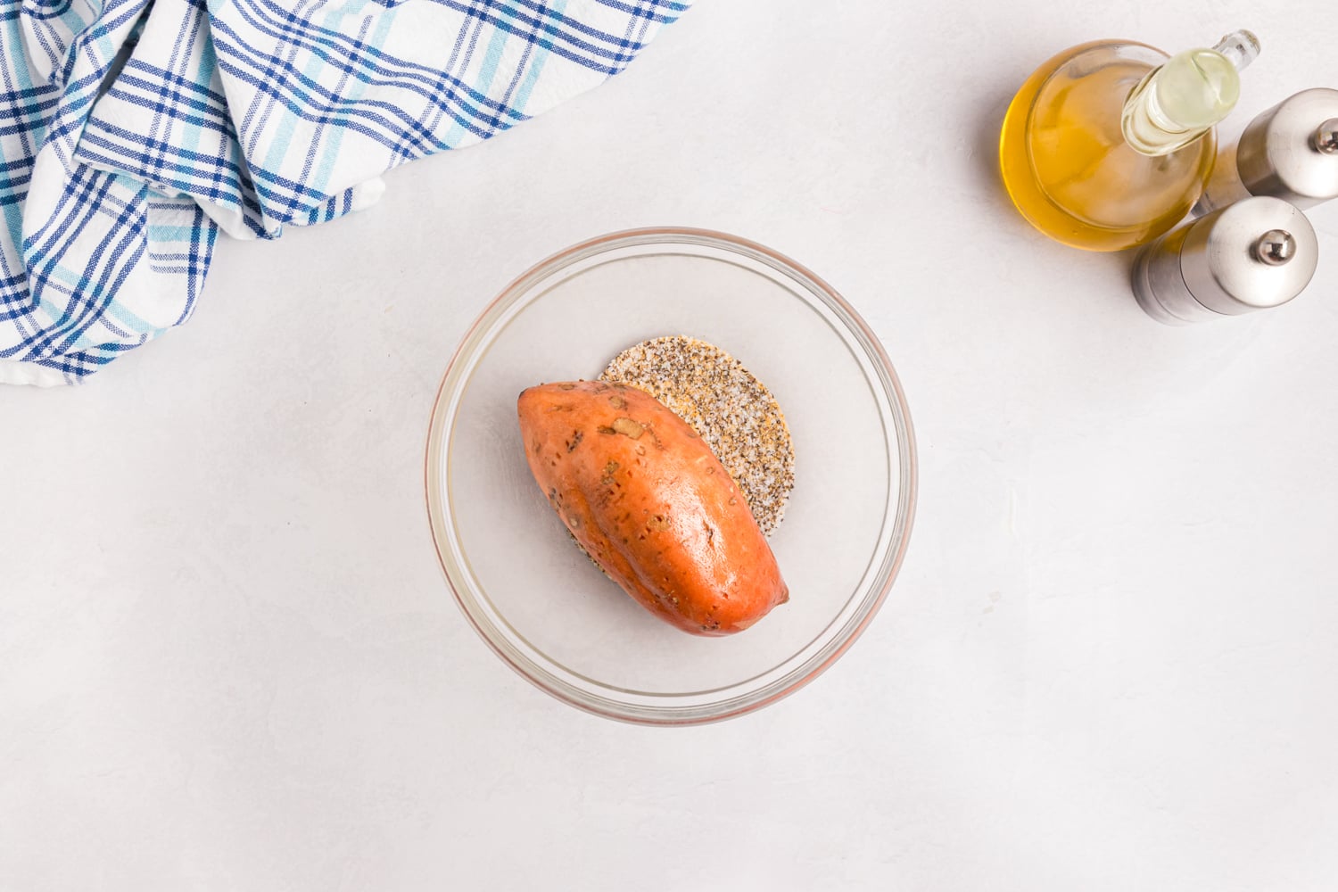 Sweet potato coated with oil and seasoning in a glass bowl.